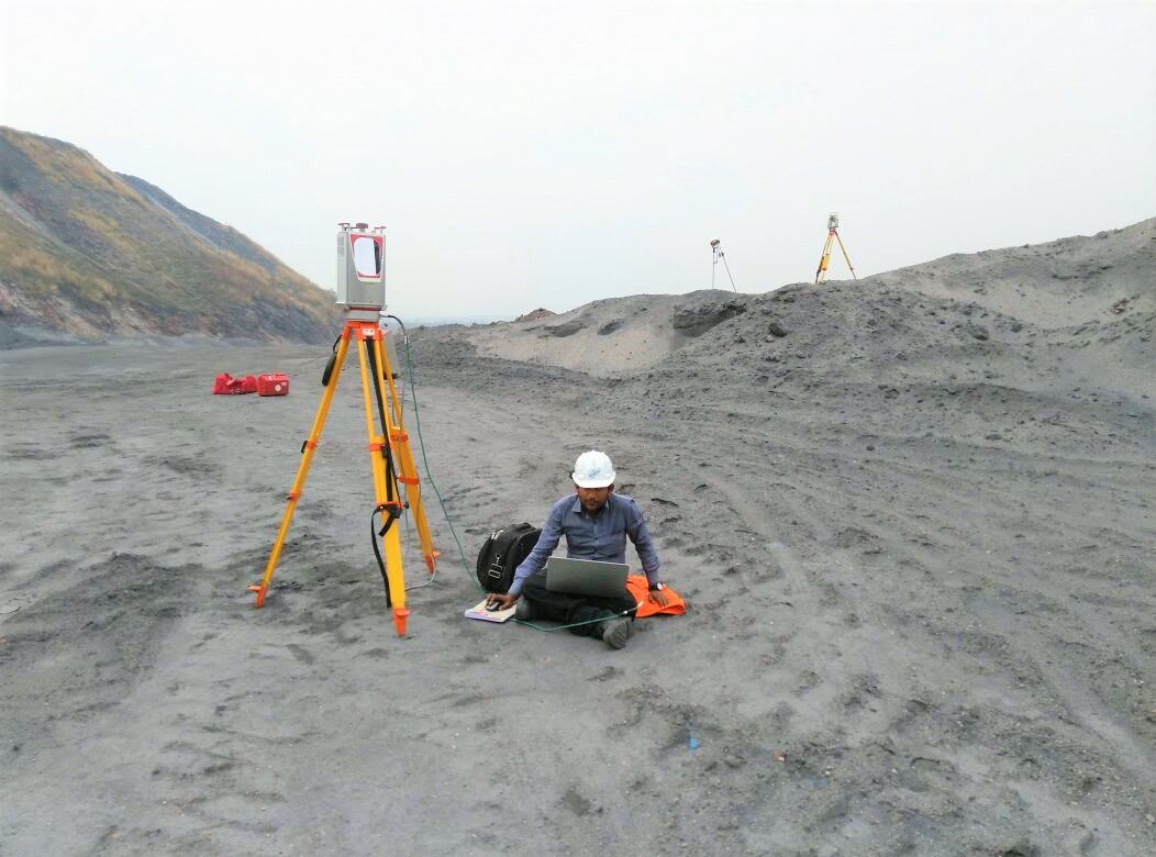Surveyor at a laptop beside a laser scanner on a tripod, open-cast mine site